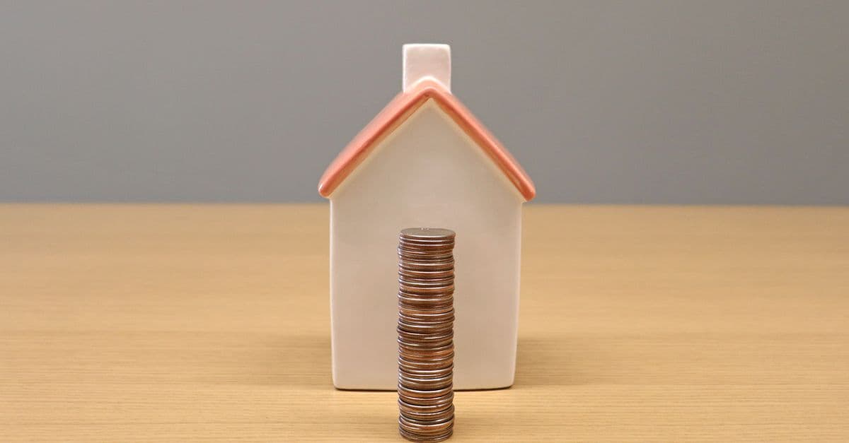 A small house model beside stacked coins