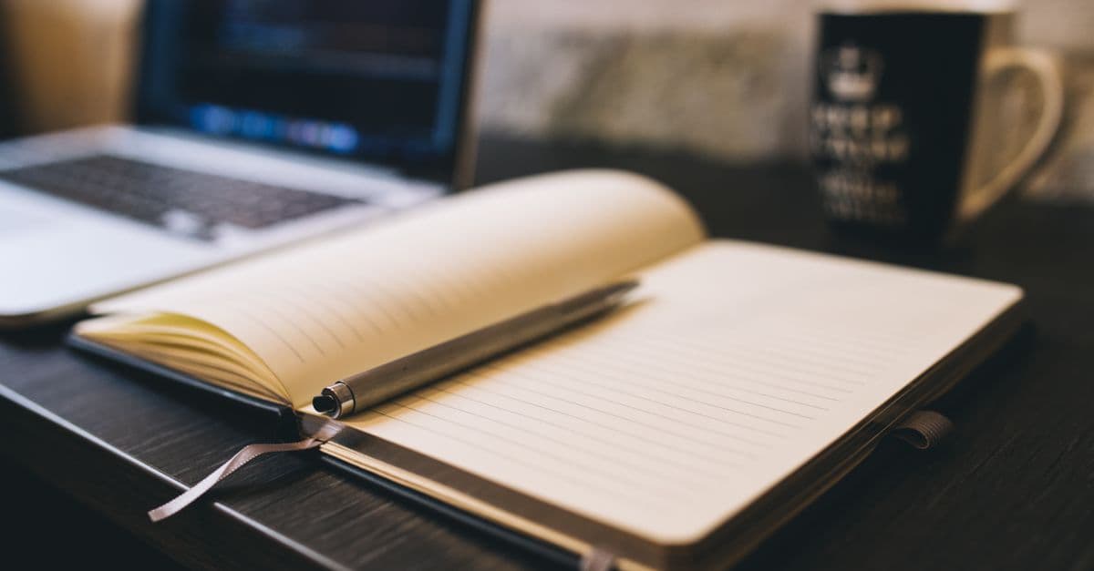 A notebook, pen and coffee on a planning desk